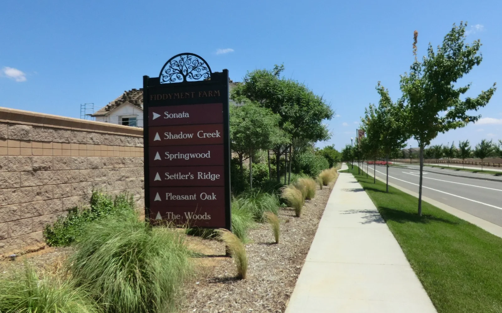 Street-level view along Hayden Parkway in Roseville: a subdivision entry sign, a house under construction behind a masonry wall, and young street trees