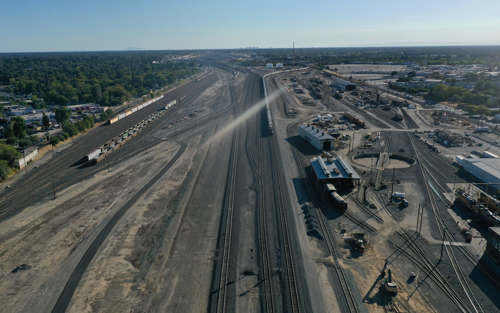 Aerial view along the Roseville rail yard, with converging tracks, lines of freight cars and yard buildings under a low sun